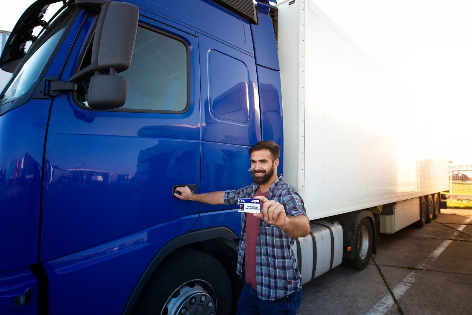 A man with his newly-acquired CDL license in front of a blue truck.